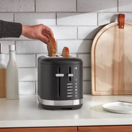 A mattfekete színű kenyérpirítóba kenyeret helyeznek.