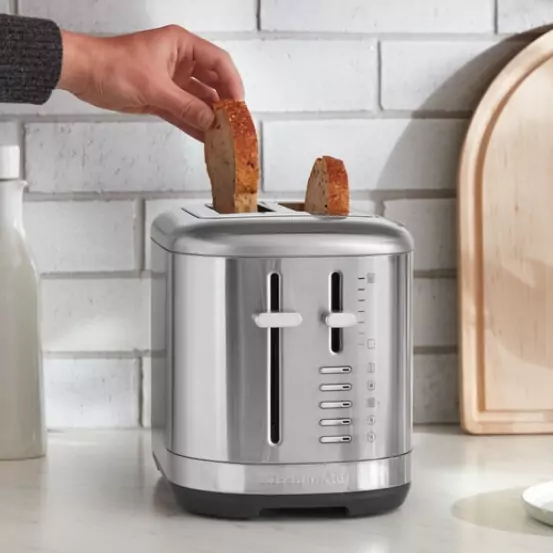 Az ezüst színű kenyérpirítóba kenyeret helyeznek.